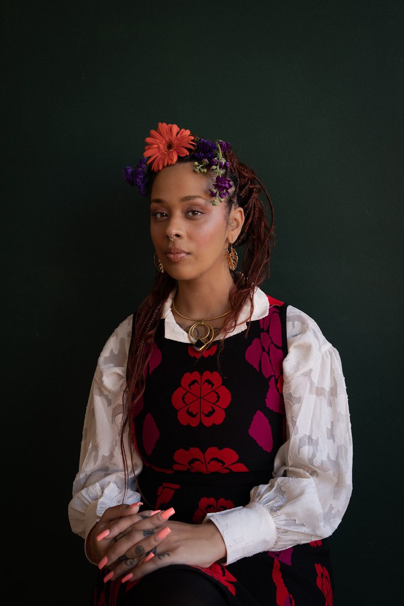 Studio portrait of a woman with flowers pinned into her braided hair, seated against a dark green backdrop