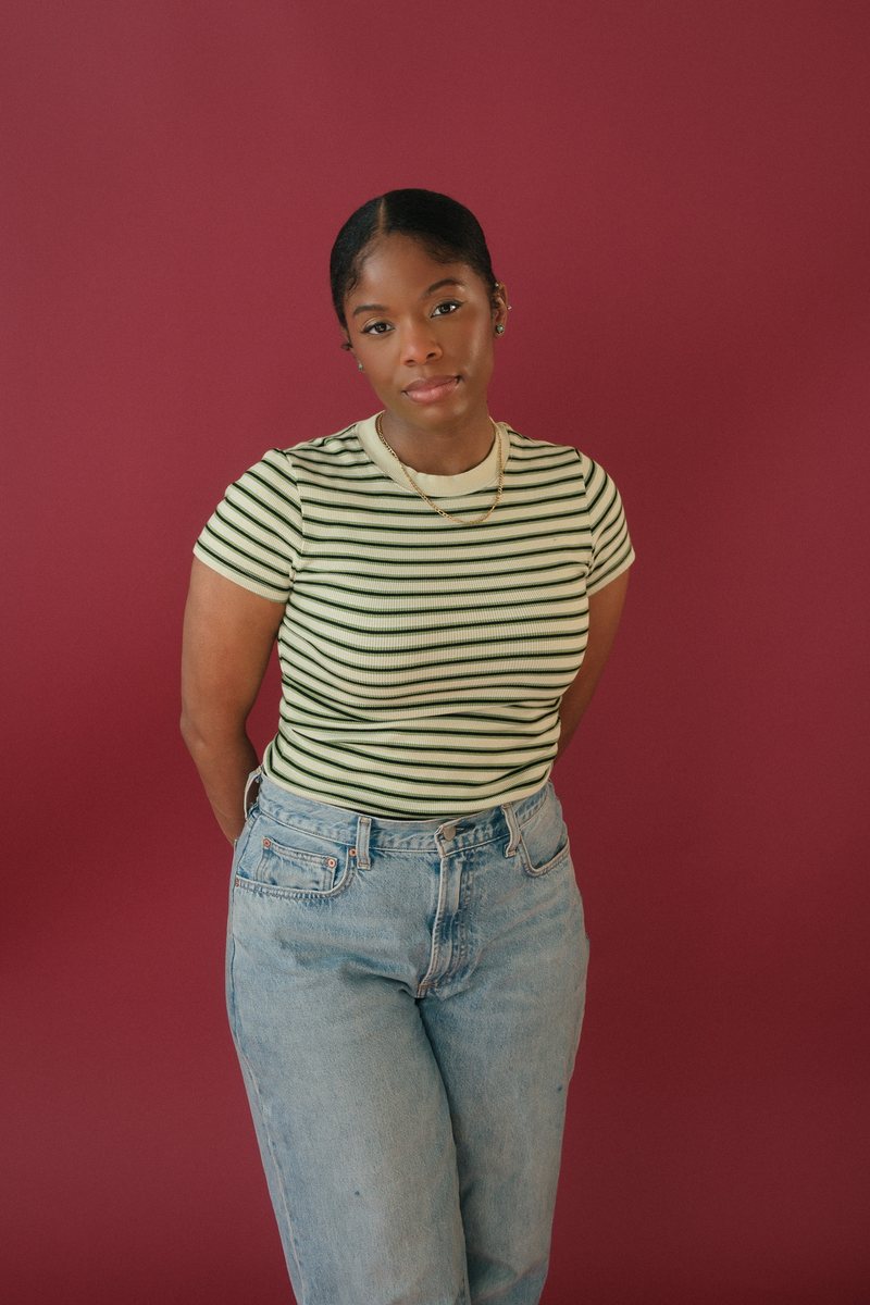 Studio portrait of a woman in a striped top and jeans, standing against a deep red backdrop
